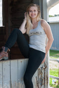 Model wears heather gray racer back tank top with Buckwild logo front paired with black riding tights while sitting on horse stall door.
